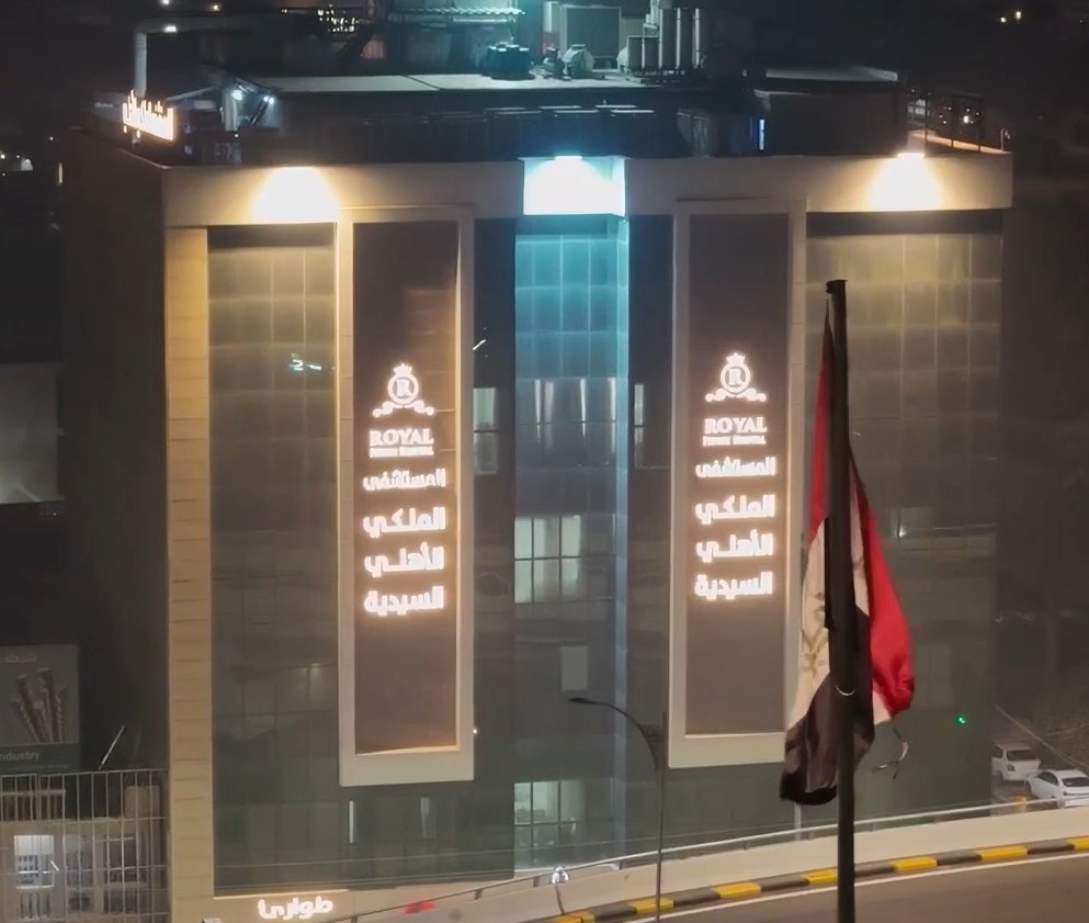 Royal Private Hospital, Al-Saidiya branch — illuminated facade signs at night beside the Iraqi flag.